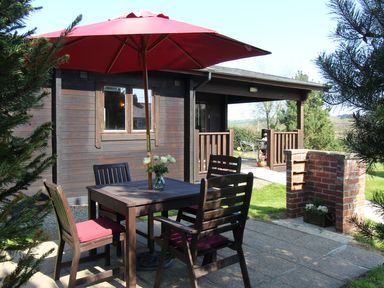 An outdoor patio area with wooden table and chairs under a red umbrella at Cherry Lodge Lanivet near Bodmin