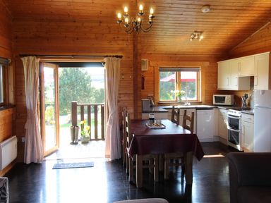 An open plan kitchen and dining area with wooden walls and ceiling a dining table with chairs and a kitchen with white cabinets at Cherry Lodge Lanivet near Bodmin