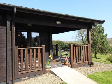 A wooden porch with two flower pots and a chair outside at Cherry Lodge in Lanivet near Bodmin