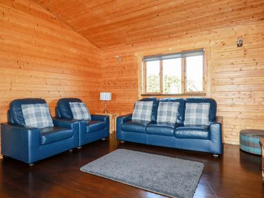 A living room with blue leather sofa and chairs and plaid cushions at Maple Lodge in Lanivet near Bodmin