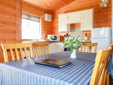 A kitchen with wooden walls and ceiling a table with a striped tablecloth and flowers in a vase at Maple Lodge in Lanivet near Bodmin