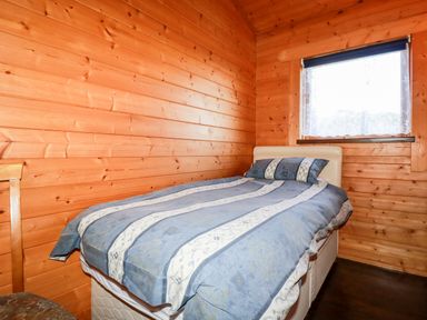 A bedroom with a bed covered in blue and white striped bedding and wooden walls at Maple Lodge Lanivet near Bodmin