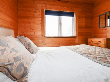 A bedroom with a bed a window with curtains and a chest of drawers at Maple Lodge in Lanivet near Bodmin