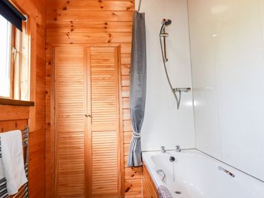 A bathroom with a wooden closet a bathtub and a shower at Maple Lodge in Lanivet near Bodmin