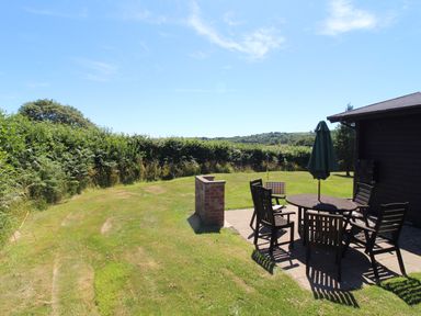 A garden with a patio table and chairs with an umbrella near a wooden structure at Maple Lodge in Lanivet near Bodmin