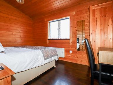 A bedroom with wooden walls a bed a desk with a black chair and a window at Cedar Lodge in Lanivet near Bodmin