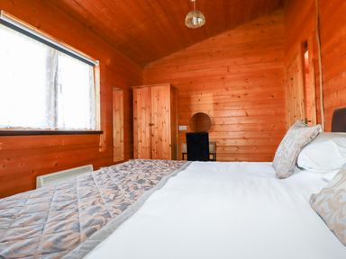 A bedroom with a bed a wardrobe a chair and a window at Cedar Lodge in Lanivet near Bodmin