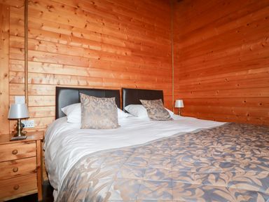 A bedroom with a double bed two patterned pillows two bedside lamps and wooden walls at Cedar Lodge Lanivet near Bodmin