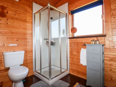 A bathroom with a shower cubicle toilet gray cabinet and window at Cedar Lodge in Lanivet near Bodmin