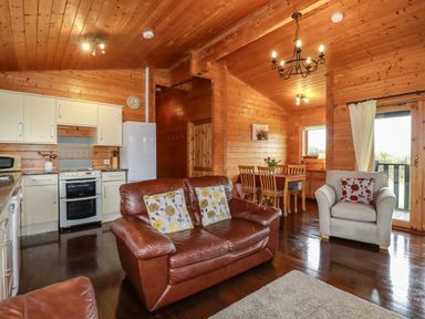 An open plan room with a kitchen dining area and seating with wooden walls and ceiling at Cedar Lodge in Lanivet near Bodmin