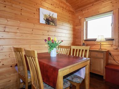 A dining area with a wooden table and chairs a vase with tulips on the table a sideboard with a lamp and wine near a window at Cedar Lodge in Lanivet near Bodmin