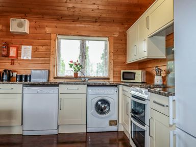 A kitchen with appliances and cabinets under a window at Cedar Lodge in Lanivet near Bodmin