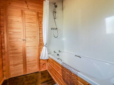 A bathroom with a bathtub shower curtain and wooden doors at Cedar Lodge Lanivet near Bodmin