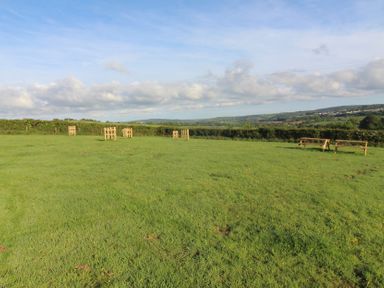 An outdoor area with wooden benches and hills in the background at Cedar Lodge in Lanivet near Bodmin