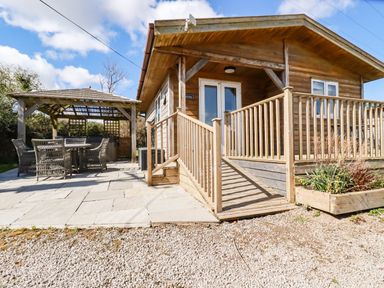 An outdoor area with a wooden cabin featuring a ramp and a patio with a covered seating area at Hunrosa in St Day