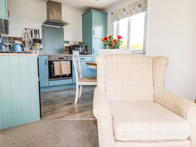 A beige armchair facing a kitchen with blue cabinets and appliances at Hunrosa in St Day