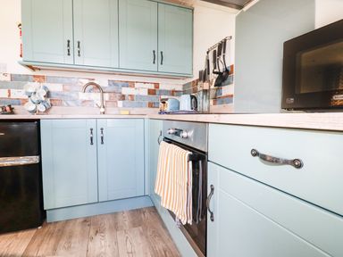 A kitchen with blue cabinets a black fridge a microwave an oven and utensils at Hunrosa in St Day