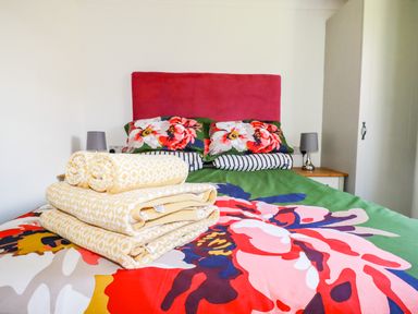 A bedroom with a bed featuring floral bedding a red headboard folded towels on the bed and two bedside tables with lamps at Hunrosa St Day