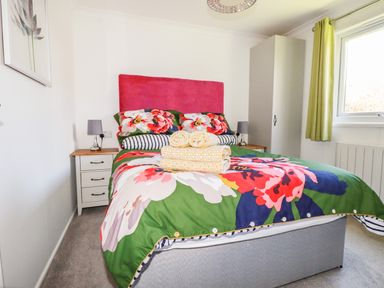 A bedroom with a double bed with floral bedding two bedside tables with lamps a wardrobe and a window with green curtains at Hunrosa in St Day