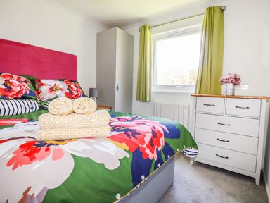 A bedroom with a bed with floral bedding and towels on it a white wardrobe green curtains and a white chest of drawers with flowers at Hunrosa St Day