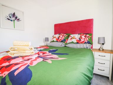 A bedroom with a double bed with floral bedding and a pink headboard with bedside tables and lamps at Hunrosa in St Day