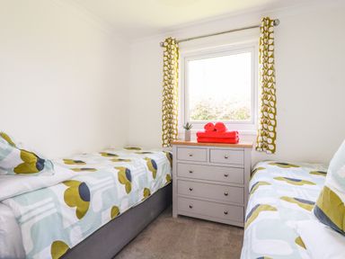 A bedroom with two single beds separated by a chest of drawers under a window with patterned curtains at Hunrosa in St Day