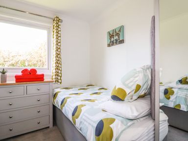 A bedroom with a bed with patterned bedding a grey chest of drawers with red towels and a small plant on top and a window with patterned curtains at Hunrosa in St Day