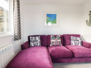 A living room with a purple sectional sofa with patterned pillows a window with curtains a radiator and a framed painting on the wall at Hunrosa St Day