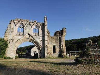 A stone archway and ruins of a historic building with a small house and trees in the background at Richmond Cottage in Burythorpe near Malton