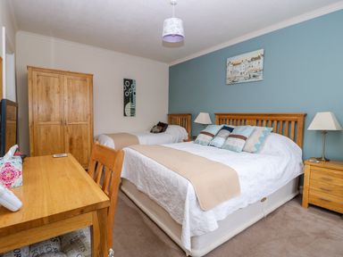 A bedroom with two beds a wooden wardrobe a desk with a chair and two bedside tables with lamps at Richmond Cottage in Burythorpe near Malton