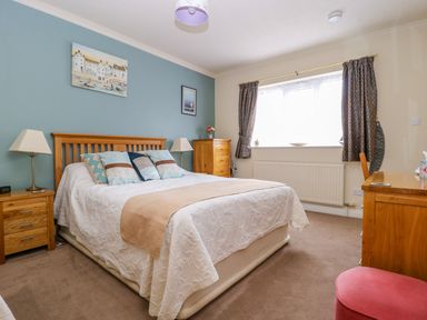 A bedroom with a double bed bedside tables lamps a chest of drawers a desk and a window with curtains at Richmond Cottage in Burythorpe near Malton