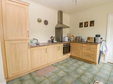 A kitchen with wooden cabinets green tiled floor and various appliances at Richmond Cottage in Burythorpe near Malton