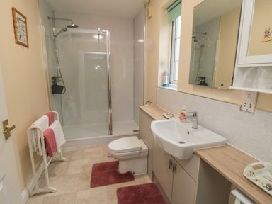 A bathroom with a shower cubicle, toilet, sink, towel rack with towels, mirror, window, and wooden countertops at Richmond Cottage in Burythorpe near Malton