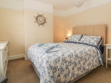 A bedroom with a bed featuring blue and white bedding towels on the bed two nightstands and a dresser at Sunvale in Teignmouth