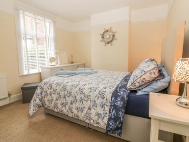 A bedroom with a bed laid with blue and white bedding a white dresser near a window and a bedside table with a lamp at Sunvale in Teignmouth
