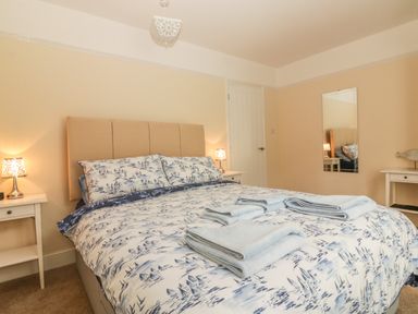 A bedroom with a double bed with printed bedding and folded towels on top and bedside tables with lamps at Sunvale in Teignmouth