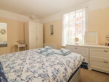 A bedroom with a bed with blue and white bedding towels on the bed a white wardrobe a white dresser and a window with blinds at Sunvale in Teignmouth