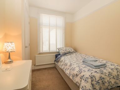 A bedroom with a single bed a bedside table with a lamp and a window with blinds at Sunvale in Teignmouth