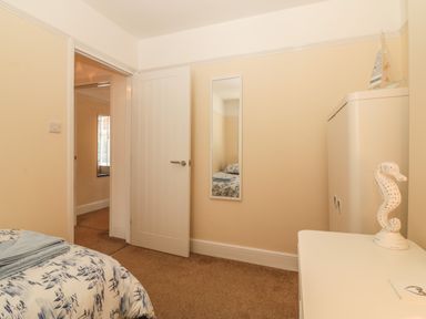 A bedroom with a bed, wall mirror, white cabinet, and seahorse decoration at Sunvale in Teignmouth