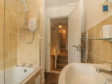 A bathroom with a bathtub shower and sink looking out to a hallway with stairs at Sunvale in Teignmouth