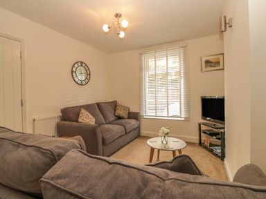A living room with gray sofas a round coffee table a wall clock and a television at Sunvale in Teignmouth