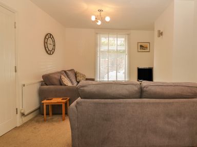A living room with grey sofas, a wooden side table, a wall clock, and a window with blinds at Sunvale in Teignmouth