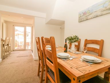 A dining area with a wooden table set with plates glasses and a bottle next to doors leading to an outdoor patio at Sunvale in Teignmouth