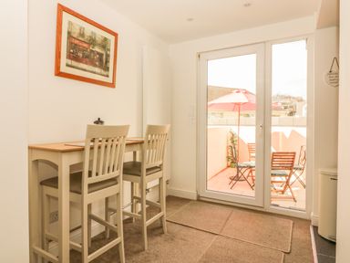 A dining area with two bar stools and a wooden table next to glass doors leading to a patio with outdoor chairs and an umbrella at Sunvale in Teignmouth