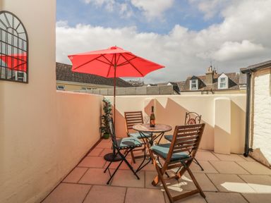 A small outdoor patio with a round table four chairs a red umbrella and buildings in the background at Sunvale in Teignmouth
