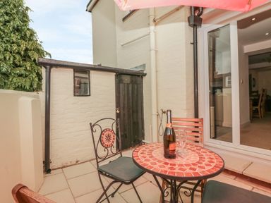 A patio with a round tiled table with a bottle and glasses and two chairs outside a building at Sunvale in Teignmouth