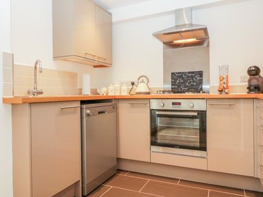 A kitchen with a sink wooden countertops cabinets a dishwasher an oven a kettle and a coffee machine at Sunvale in Teignmouth