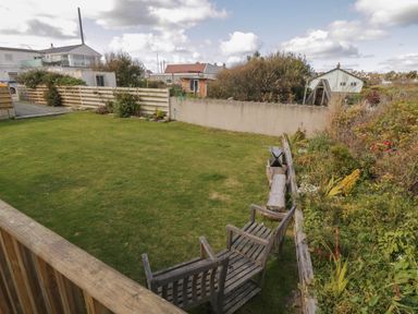 A garden with two wooden benches on grass and a flower bed next to a low wall at Coed Llai Lodge in Trearddur Bay