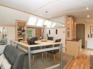 A dining area with a round table and four chairs next to wooden cabinets and skylight windows at Coed Llai Lodge in Trearddur Bay