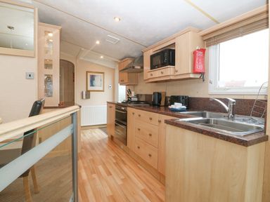 A kitchen with wooden cabinets sink and cooking appliances at Coed Llai Lodge in Trearddur Bay